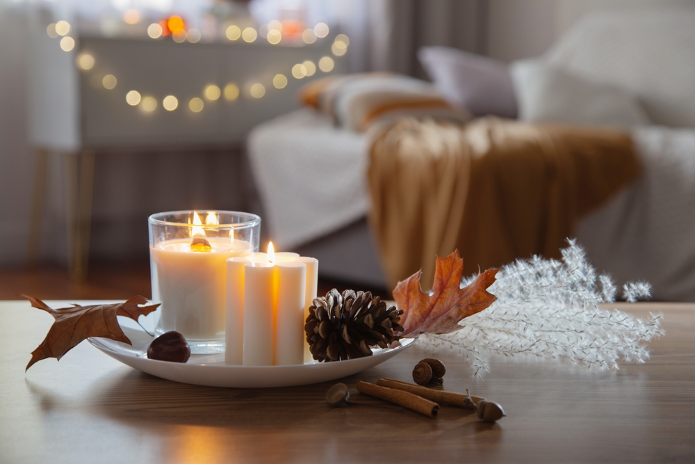 Imagen de una decoración de un salón en otoño de una vivienda, con velas, piñas y hojas caídas.